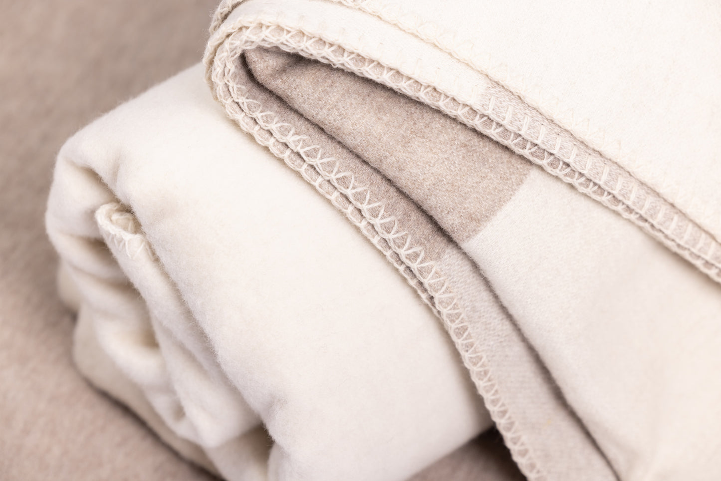 This is a 100% sheep wool throw blanket with a warm and inviting design. It features a large checkered pattern in neutral tones of beige and cream, offering a classic and timeless aesthetic.