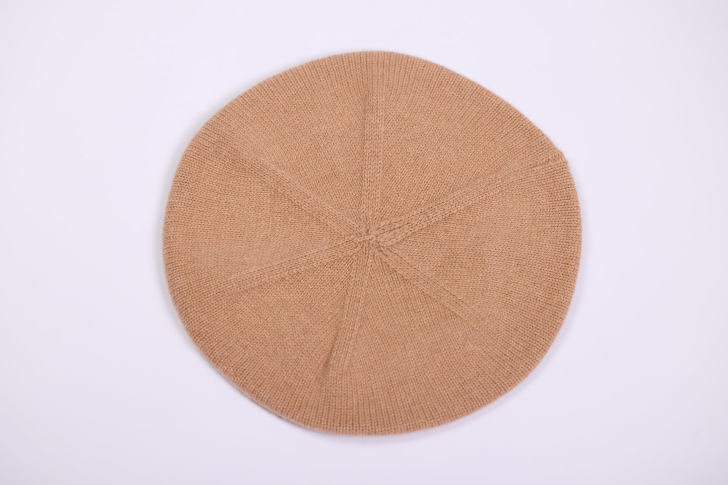 This image showcases a classic cashmere beret in a camel color, photographed flat to highlight its round, soft structure. The beret features a smooth, fine-knit finish that emphasizes the luxurious softness of the cashmere material. Its lightweight design and seamless construction provide both comfort and elegance.