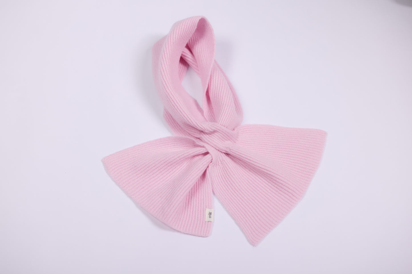 This small cashmere scarf in a soft, elegant and simple. The scarf is ribbed, giving it a subtle texture that adds depth to its appearance while maintaining a refined look. The style is minimalist, and it’s knotted in a chic bow-like manner, providing a cozy yet polished touch around the neck.