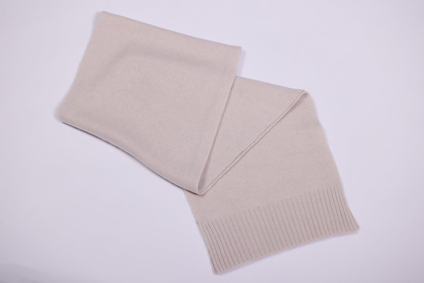 This image shows a long knitted scarf made of cashmere. It is light beige, featuring a smooth, soft texture characteristic of cashmere material. The scarf has ribbed detailing at the ends, providing a subtle design element. The scarf appears cozy and versatile, suitable for both casual and formal wear.