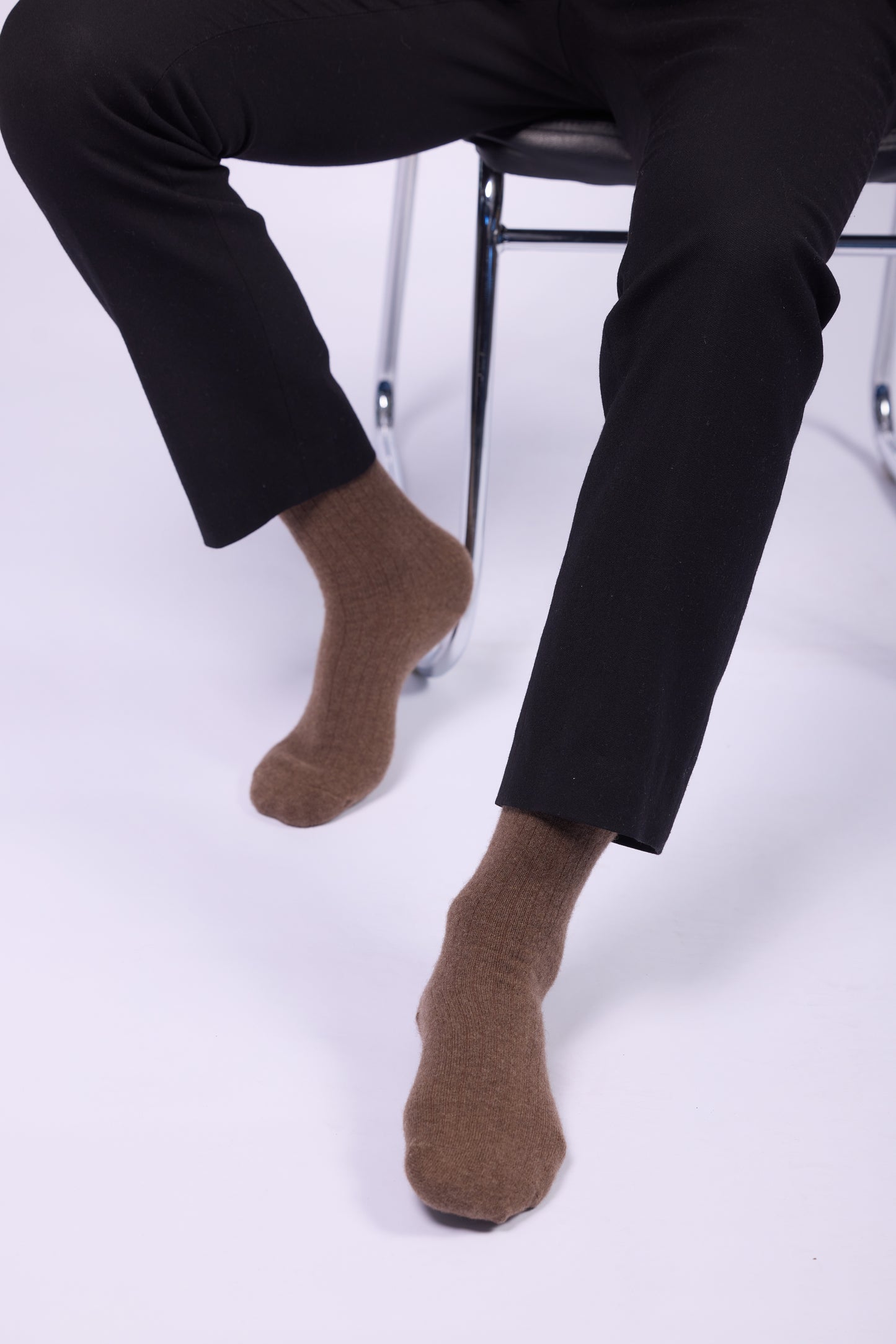 These brown yak wool socks are showcased on a person sitting on a chair. The socks appear thick, soft, and plush, ideal for providing warmth and comfort during cold weather. The material has a ribbed texture that gives the socks a stylish yet practical look. The earthy brown tone complements the black trousers worn by the individual, adding a subtle, natural contrast. Yak wool is renowned for its insulating properties, softness, and durability, making these socks a premium choice.