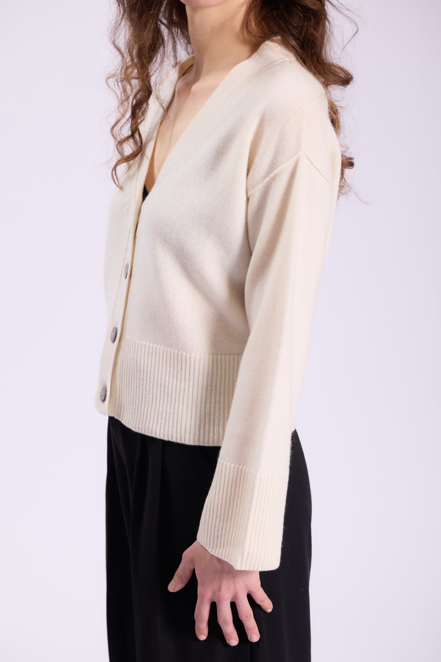 This image features a chic white cashmere cardigan styled in a modern, relaxed fit. The cardigan has a clean, minimalist design with a V-neckline and long sleeves, making it both versatile and timeless. The fabric appears soft, smooth, and finely knit, highlighting the luxurious quality of cashmere.
The cardigan is adorned with a row of elegant buttons down the front, adding a subtle, polished touch. The ribbed cuffs and hem provide structure to the silhouette while maintaining comfort.
