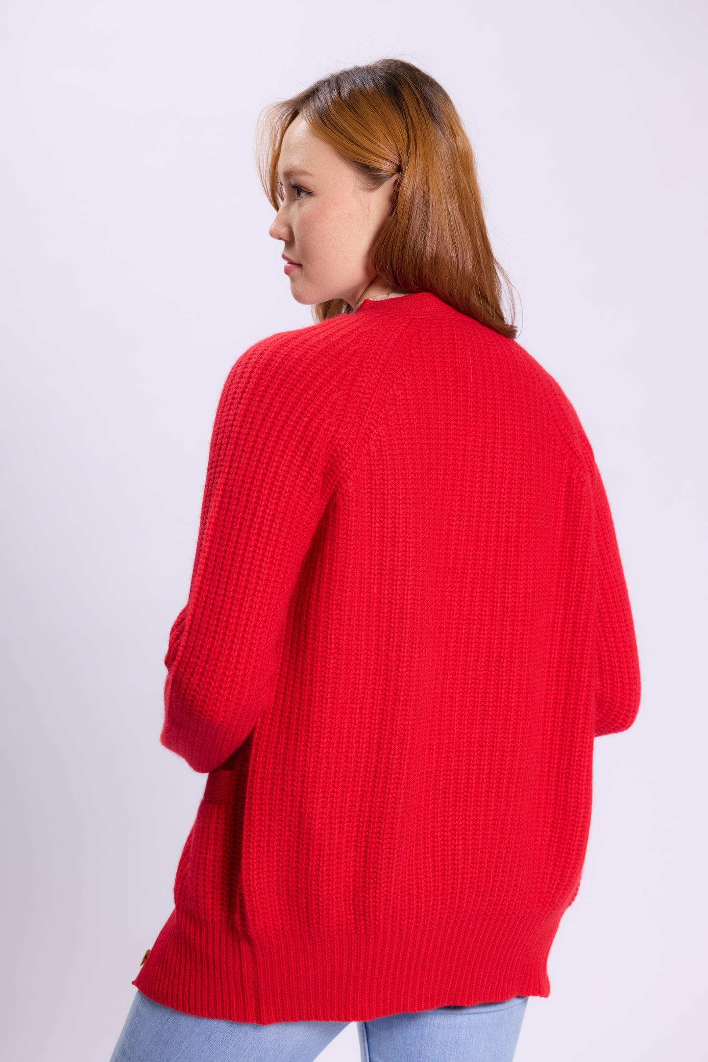 This is a long, thick knit cardigan made of cashmere in a bright red color. It features a textured design with a relaxed fit, making it cozy and stylish for cooler weather. The cardigan has a V-neckline, long sleeves, and a button-up front with shiny, silver-toned buttons that add a subtle touch of elegance.