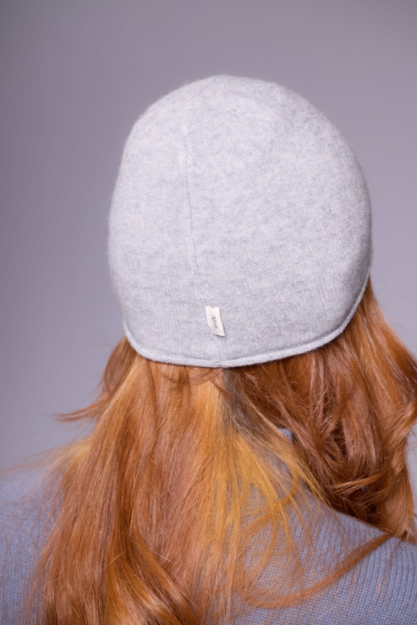This image features a lightweight, thin cashmere hat in a light grey color. The hat has a minimalist design, with a snug fit that contours smoothly to the head, offering a sleek and understated look.
