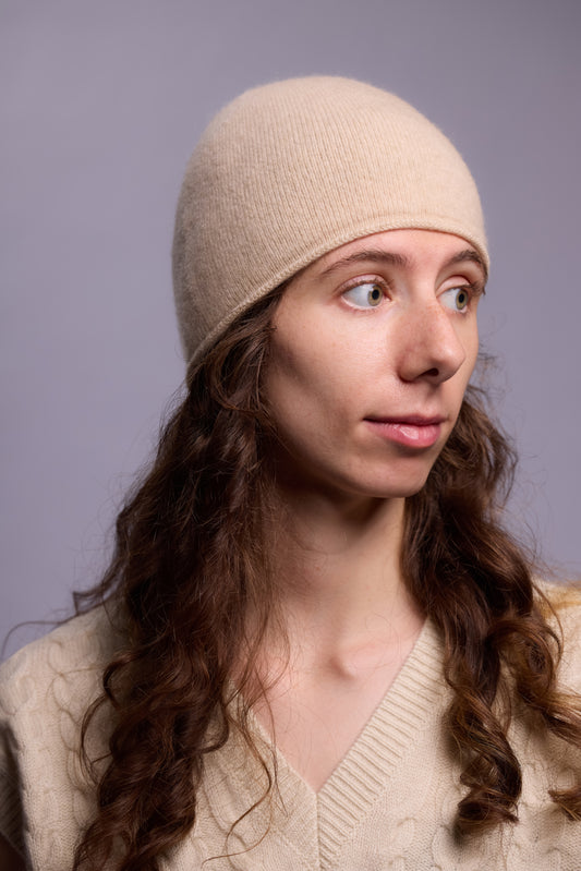 This image features a lightweight, thin cashmere hat in a soft beige color. The hat has a minimalist design, with a snug fit that contours smoothly to the head, offering a sleek and understated look. 
