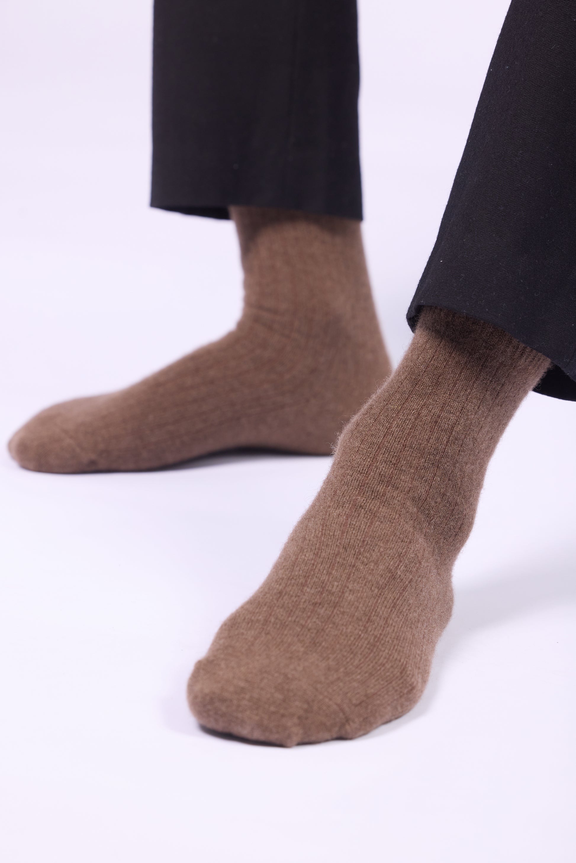 These are brown yak wool socks, characterized by a ribbed texture and a soft, thick, and plush appearance. The wool looks cozy and warm, ideal for colder climates. The socks reach the lower calf and are paired with black trousers in the image, providing a contrast to their natural, earthy tone. Yak wool is known for its durability, warmth, and softness, making these socks both practical and luxurious.