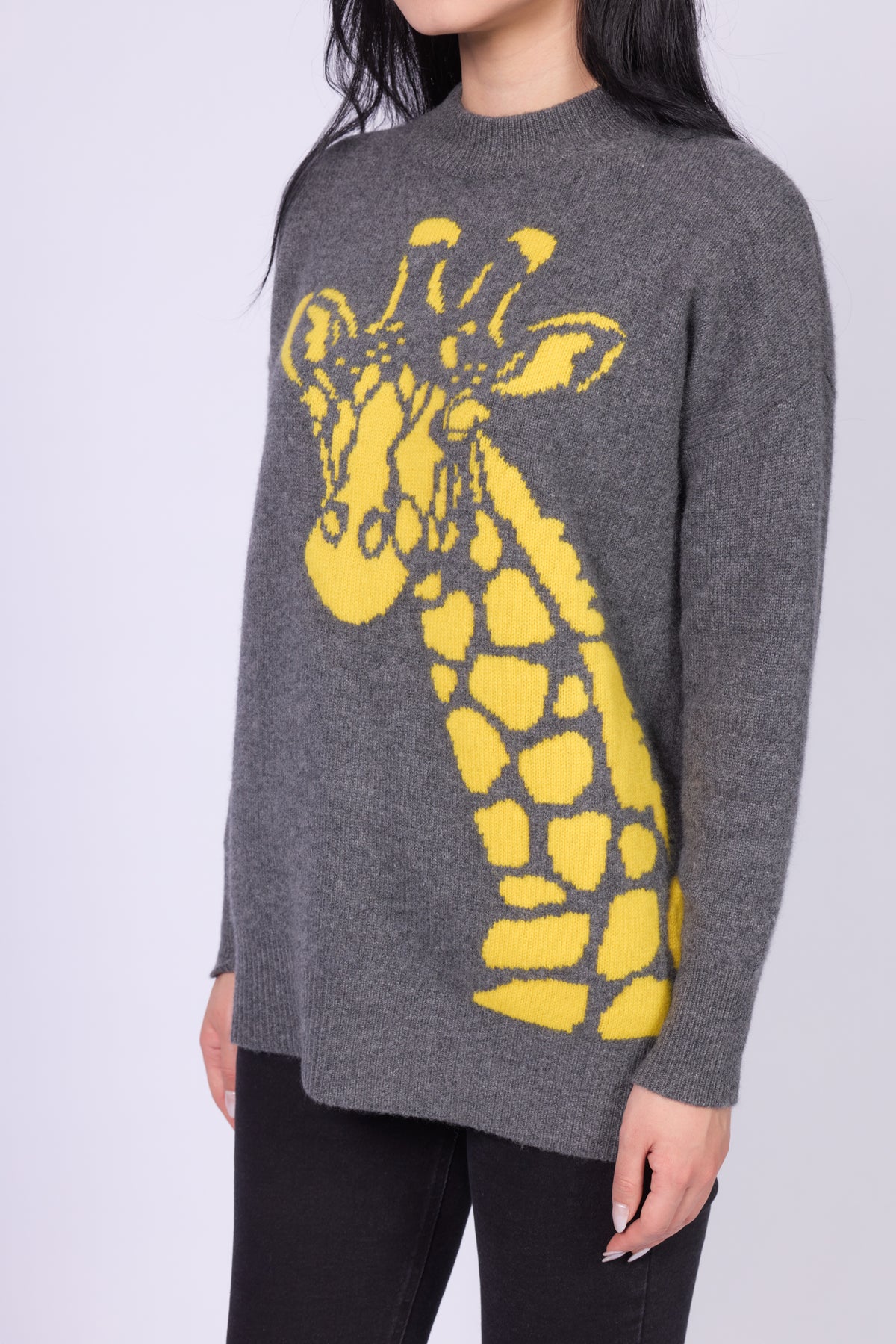 This is a stylish women's cashmere sweater featuring a bold, playful giraffe design in bright yellow. The sweater is a relaxed fit with a classic crew neckline and long sleeves. 